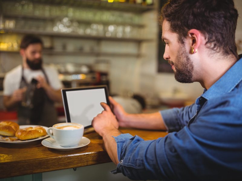 Man using digital tablet while having coffee in café Man sitting at counter and using digital tablet while having coffee in café